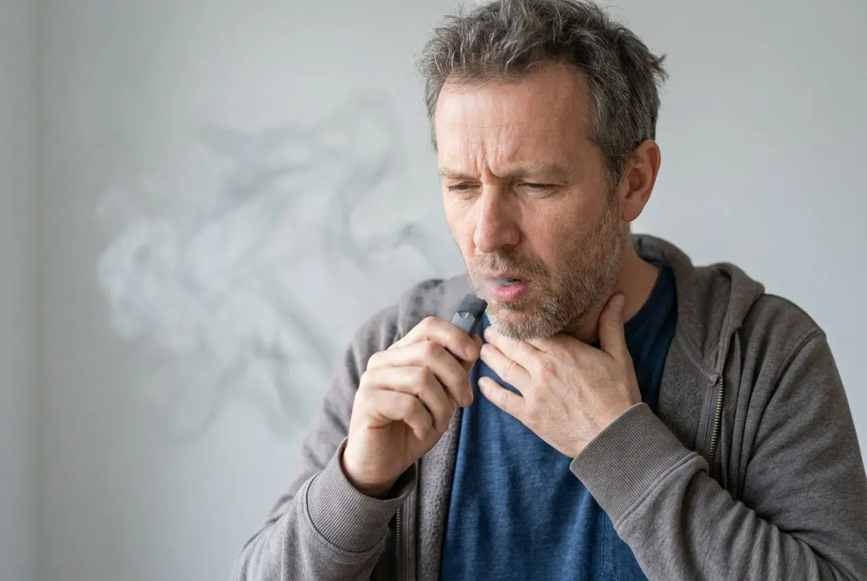 Homme utilisant un e‑cigarette, expression de douleur en gorge, fumée légère autour, illustration du sujet “e liquide qui brûle.la.gorge” et de l’inconfort lié au hit.